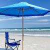 A blue beach umbrella casts shade over a blue folding chair on a sunny beach