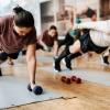 Female friends exercise with dumbbells on mats in a gym class