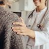 A female doctor in a white lab coat rests a comforting hand on a patient's shoulder