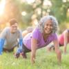 A small group of people do pushups in the grass at a park