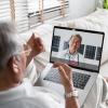 An older adult male wearing glasses talks with a doctor during a video call on a laptop