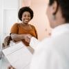A woman arriving at a medical office smiles and shakes hands with a female doctor