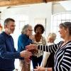 A friendly gathering of mature adults greets one another with hugs and conversation