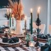 A festive table decorated with a green-checkered table cloth, candles, dinner plates and folded napkins.