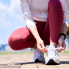 A runner in red athletic leggings ties her sneaker's laces
