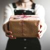 An unseen person presents a gift box wrapped in candy-cane gift paper