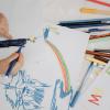 Child's small hands hold a marker while creating a colorful drawing